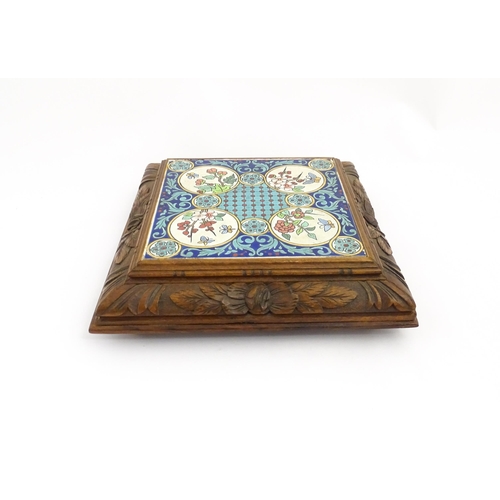 1287 - A 20thC carved wooden teapot stand set with Longwy tile to top having floral and foliate decoration,... 