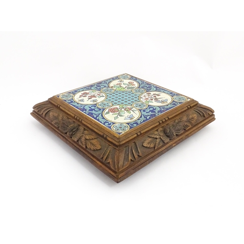 1287 - A 20thC carved wooden teapot stand set with Longwy tile to top having floral and foliate decoration,... 