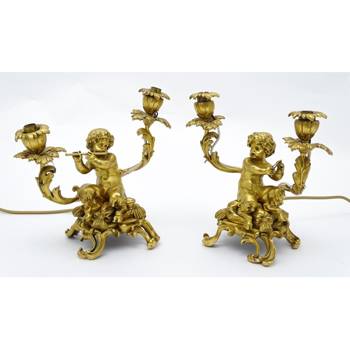 1532 - A pair of Continental gilt bronze twin branch table lamps, each modelled as a seated faun playing a ... 