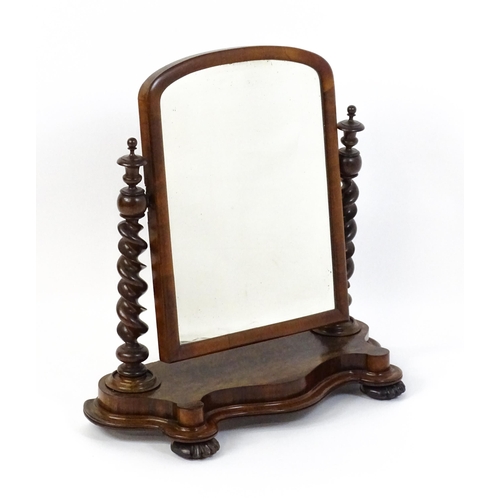 1565 - A Victorian mahogany mirror with two barley twist supports above a shaped, moulded base raised on sq... 