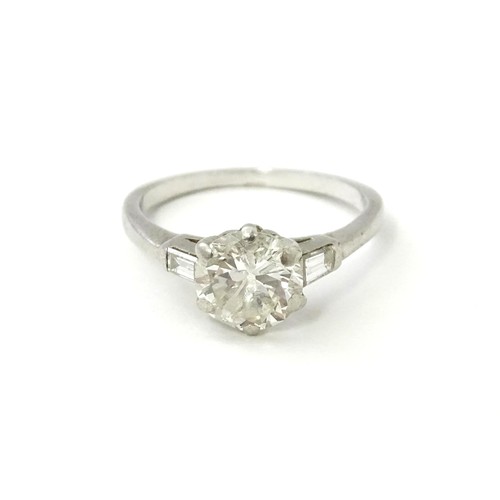 567 - A platinum set brilliant diamond solitaire ring flanked by two baguette cut diamonds to shoulders. C... 