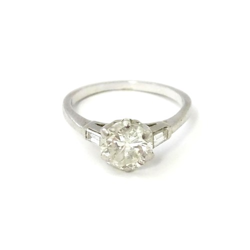 567 - A platinum set brilliant diamond solitaire ring flanked by two baguette cut diamonds to shoulders. C... 