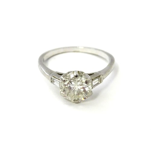 567 - A platinum set brilliant diamond solitaire ring flanked by two baguette cut diamonds to shoulders. C... 