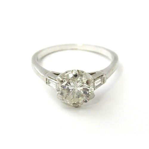 567 - A platinum set brilliant diamond solitaire ring flanked by two baguette cut diamonds to shoulders. C... 