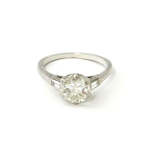 567 - A platinum set brilliant diamond solitaire ring flanked by two baguette cut diamonds to shoulders. C... 