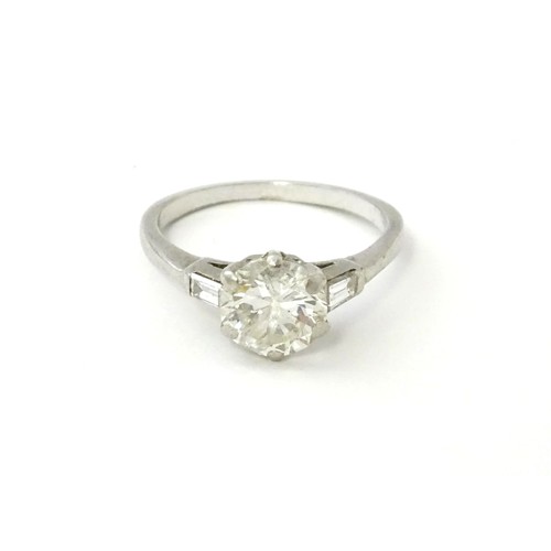 567 - A platinum set brilliant diamond solitaire ring flanked by two baguette cut diamonds to shoulders. C... 