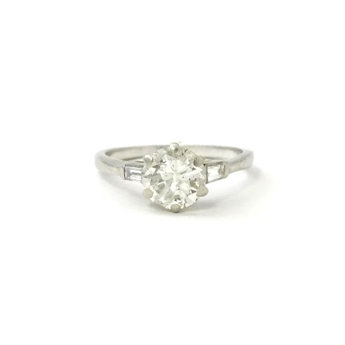 567 - A platinum set brilliant diamond solitaire ring flanked by two baguette cut diamonds to shoulders. C... 