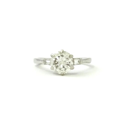 567 - A platinum set brilliant diamond solitaire ring flanked by two baguette cut diamonds to shoulders. C... 