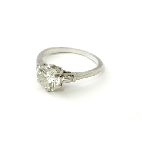 567 - A platinum set brilliant diamond solitaire ring flanked by two baguette cut diamonds to shoulders. C... 