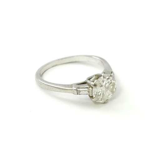 567 - A platinum set brilliant diamond solitaire ring flanked by two baguette cut diamonds to shoulders. C... 