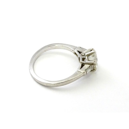 567 - A platinum set brilliant diamond solitaire ring flanked by two baguette cut diamonds to shoulders. C... 