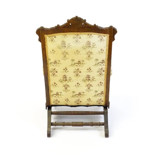 643 - An early 20thC rocking chair with carved cresting rail above a chamfered frame, with upholstered bac... 