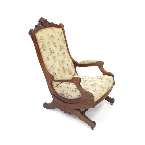643 - An early 20thC rocking chair with carved cresting rail above a chamfered frame, with upholstered bac... 