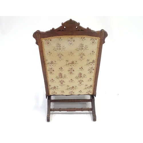 643 - An early 20thC rocking chair with carved cresting rail above a chamfered frame, with upholstered bac... 