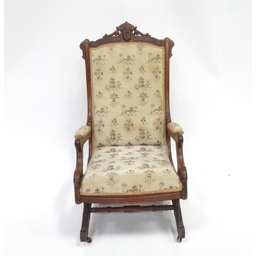 643 - An early 20thC rocking chair with carved cresting rail above a chamfered frame, with upholstered bac... 