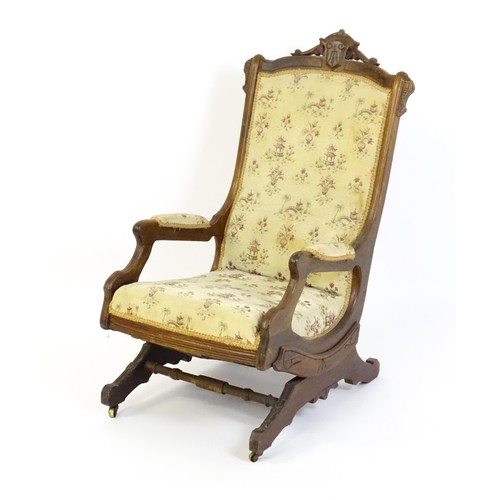 643 - An early 20thC rocking chair with carved cresting rail above a chamfered frame, with upholstered bac... 