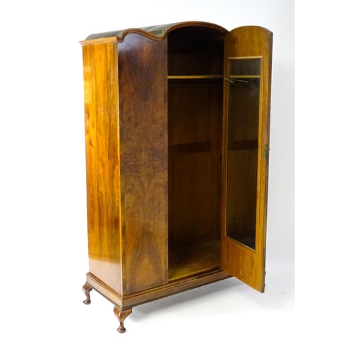 645 - An Art Deco style walnut wardrobe with a shaped cornice above a single panelled door raised on a det... 