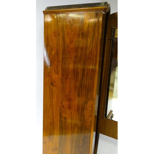 645 - An Art Deco style walnut wardrobe with a shaped cornice above a single panelled door raised on a det... 