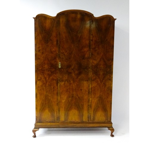 645 - An Art Deco style walnut wardrobe with a shaped cornice above a single panelled door raised on a det... 