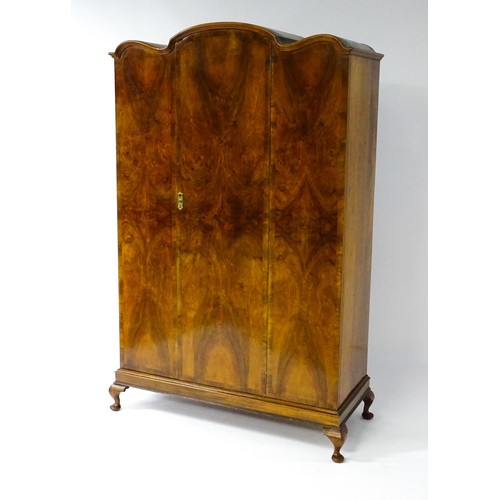 645 - An Art Deco style walnut wardrobe with a shaped cornice above a single panelled door raised on a det... 
