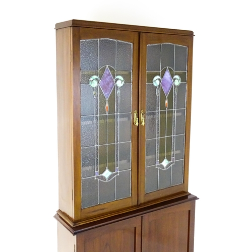 763 - An early / mid 20thC mahogany bookcase with stained and leaded glass panels above two panelled cupbo... 