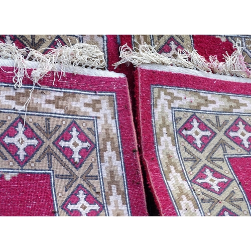 704 - Carpets/ Rugs :  Three red ground rugs with repeating geometric motifs.  Approx 37