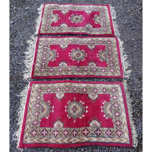 704 - Carpets/ Rugs :  Three red ground rugs with repeating geometric motifs.  Approx 37