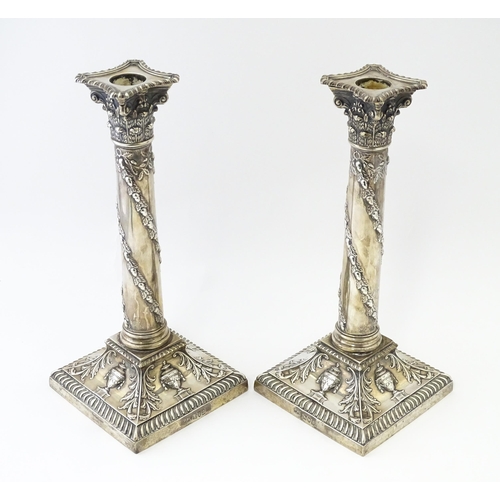 545 - A pair of Edwardian silver candlesticks of column form with urn, acanthus, and acorn and oak leaf ga... 