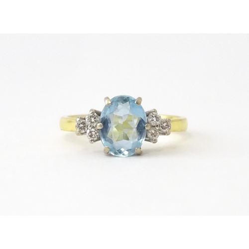 631 - An 18ct gold ring set with a central aquamarine flanked by diamonds. Ring size approx. M