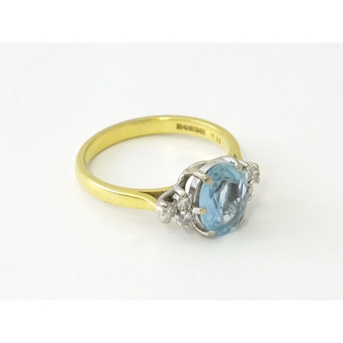 631 - An 18ct gold ring set with a central aquamarine flanked by diamonds. Ring size approx. M