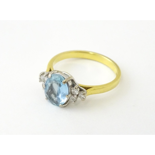 631 - An 18ct gold ring set with a central aquamarine flanked by diamonds. Ring size approx. M