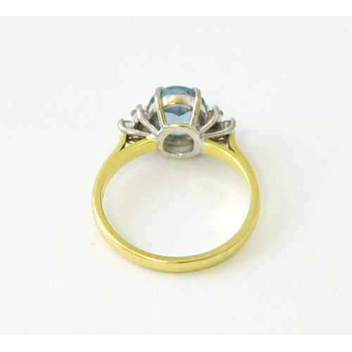 631 - An 18ct gold ring set with a central aquamarine flanked by diamonds. Ring size approx. M