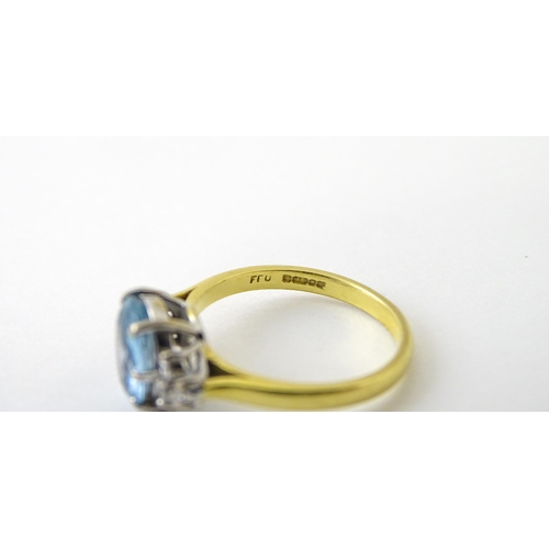 631 - An 18ct gold ring set with a central aquamarine flanked by diamonds. Ring size approx. M