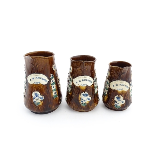 59 - A set of three Victorian Measham bargeware graduated jugs decorated with flowers and foliage, each b... 