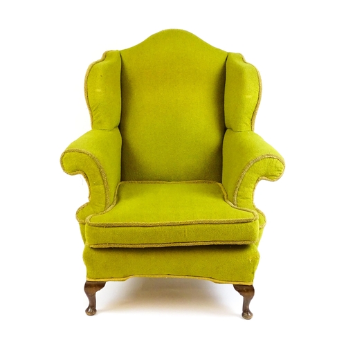 1568 - An Edwardian wingback armchair with scrolled arms and raised on short cabriole legs terminating in p... 