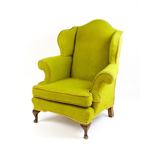 1568 - An Edwardian wingback armchair with scrolled arms and raised on short cabriole legs terminating in p... 