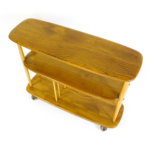 1650 - Vintage / Retro: An Ercol elm trolley with three shaped tiers on four turned supports and raised on ... 