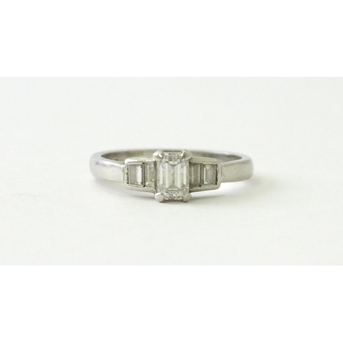 626 - A platinum ring set with a central baguette cut diamond flanked by two further diamonds to each shou... 