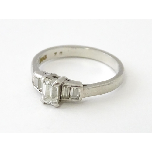 626 - A platinum ring set with a central baguette cut diamond flanked by two further diamonds to each shou... 