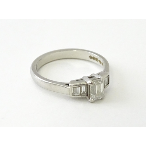 626 - A platinum ring set with a central baguette cut diamond flanked by two further diamonds to each shou... 