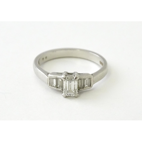 626 - A platinum ring set with a central baguette cut diamond flanked by two further diamonds to each shou... 