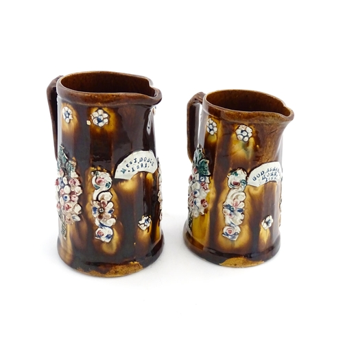 150 - Two Victorian Measham bargeware jugs decorated with flower detail, each bearing a plaque one titled ... 