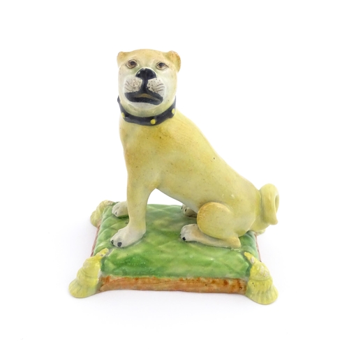 55 - A 19thC model of a Pug dog seated on a green tasselled cushion. Approx. 4 1/2