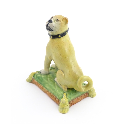 55 - A 19thC model of a Pug dog seated on a green tasselled cushion. Approx. 4 1/2