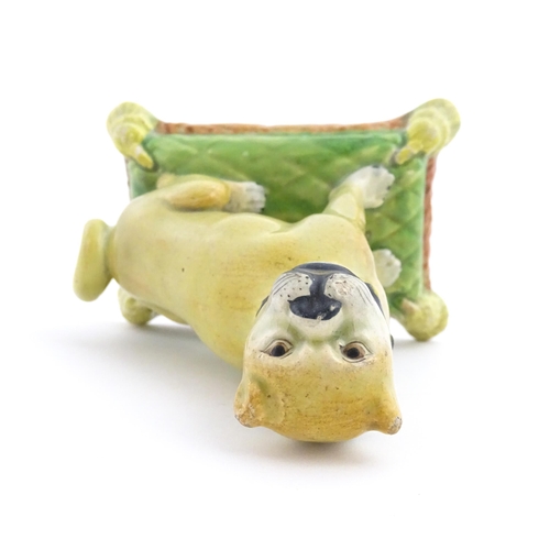 55 - A 19thC model of a Pug dog seated on a green tasselled cushion. Approx. 4 1/2