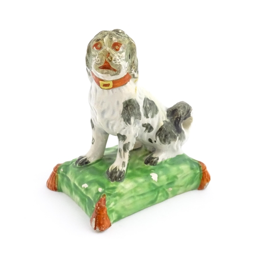 56 - A 19thC model of a seated dog with a red collar on a green tasselled cushion. Approx. 3 3/4