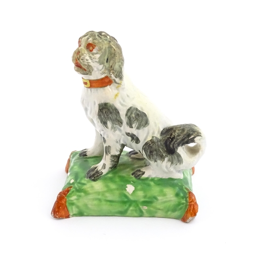 56 - A 19thC model of a seated dog with a red collar on a green tasselled cushion. Approx. 3 3/4