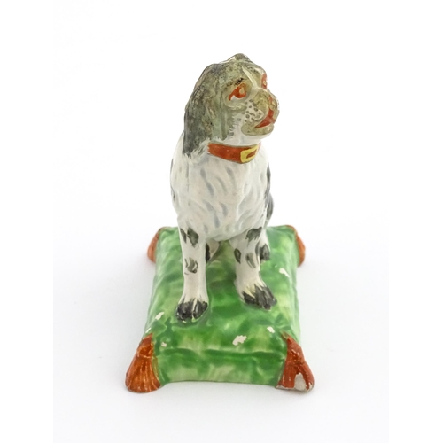 56 - A 19thC model of a seated dog with a red collar on a green tasselled cushion. Approx. 3 3/4