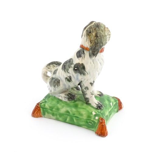 56 - A 19thC model of a seated dog with a red collar on a green tasselled cushion. Approx. 3 3/4