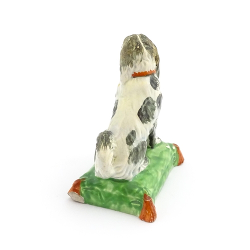 56 - A 19thC model of a seated dog with a red collar on a green tasselled cushion. Approx. 3 3/4